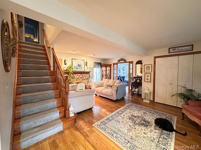 living room featuring arched walkways, beamed ceiling, stairway, and wood finished floors