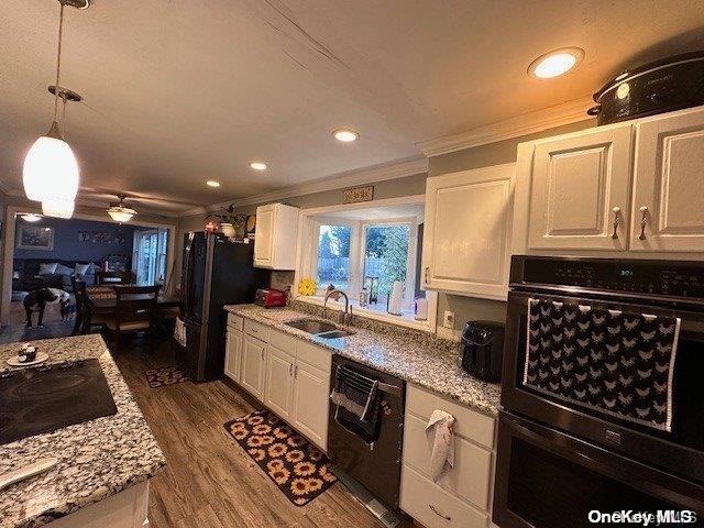 kitchen with a sink, white cabinets, dark wood-style floors, black appliances, and crown molding