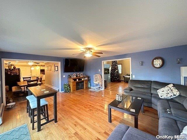 living area with light wood-style floors, a baseboard heating unit, and ceiling fan