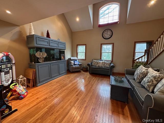 living room with high vaulted ceiling, light wood-style flooring, and stairway