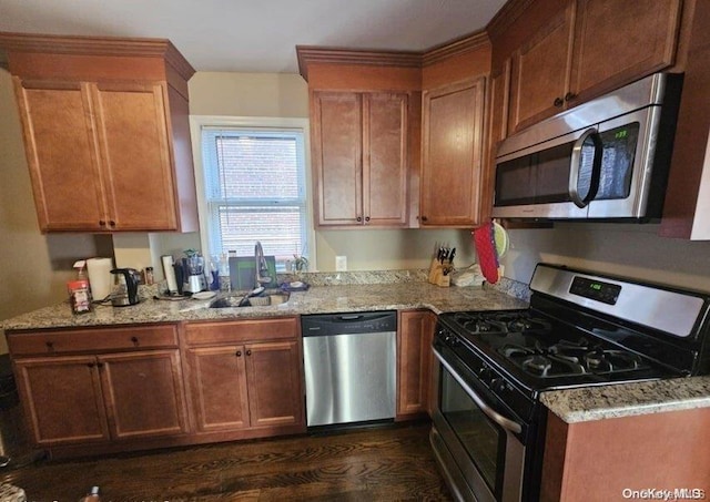 kitchen with appliances with stainless steel finishes, light stone counters, dark wood-type flooring, and sink