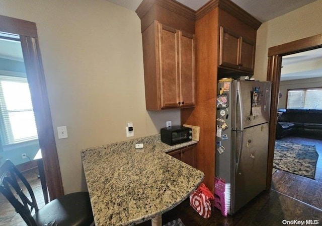 kitchen with stainless steel refrigerator, light stone counters, dark hardwood / wood-style floors, kitchen peninsula, and a breakfast bar area