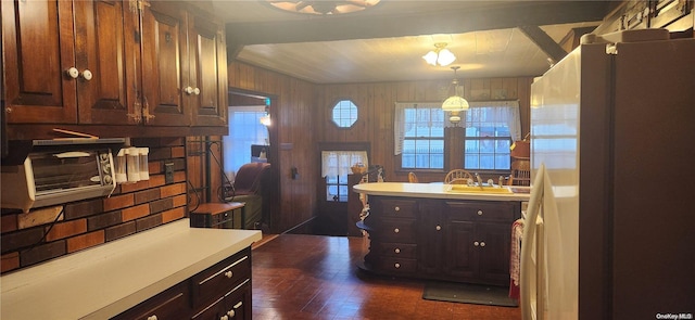 kitchen featuring white refrigerator, dark brown cabinetry, sink, and wooden walls