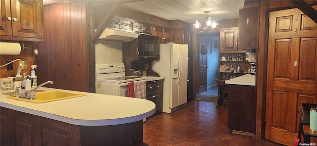 kitchen featuring white appliances, hanging light fixtures, sink, wooden walls, and a chandelier