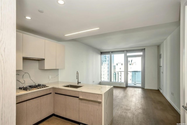 kitchen with kitchen peninsula, light stone countertops, sink, light hardwood / wood-style flooring, and stainless steel gas stovetop