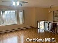 empty room with baseboard heating, ceiling fan, a healthy amount of sunlight, and hardwood / wood-style flooring