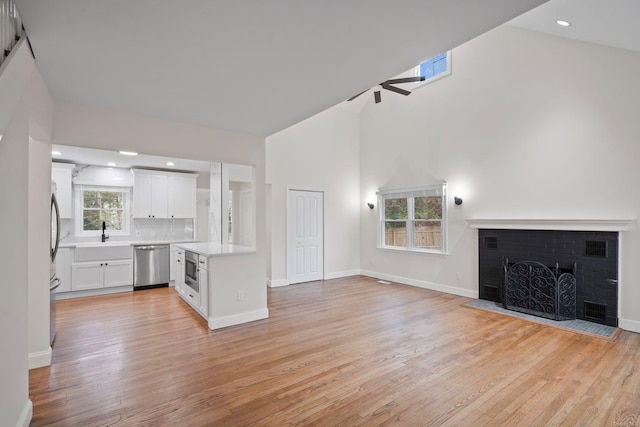 unfurnished living room with baseboards, light wood-style floors, a brick fireplace, and high vaulted ceiling