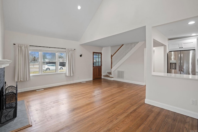 unfurnished living room with visible vents, light wood-type flooring, a fireplace, baseboards, and stairs