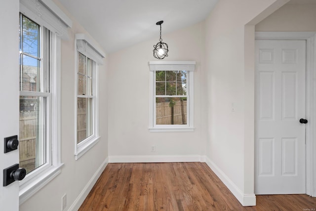 unfurnished dining area featuring baseboards, wood finished floors, and vaulted ceiling