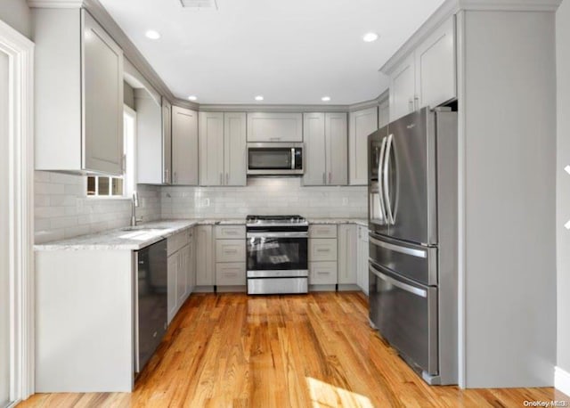 kitchen featuring gray cabinetry, light stone countertops, appliances with stainless steel finishes, and light hardwood / wood-style flooring