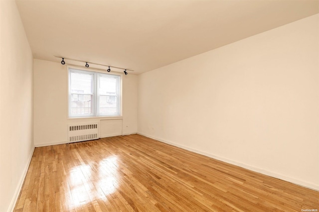 unfurnished room with light hardwood / wood-style floors, radiator heating unit, and track lighting