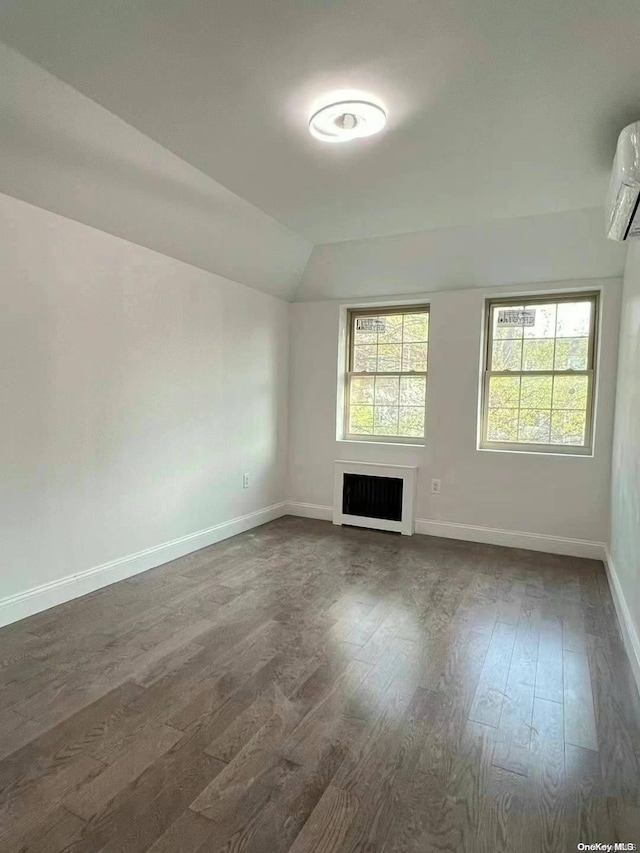 empty room with dark hardwood / wood-style floors, a wall unit AC, heating unit, and lofted ceiling