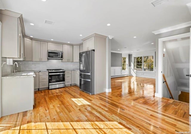 kitchen with appliances with stainless steel finishes, backsplash, gray cabinets, and light hardwood / wood-style flooring