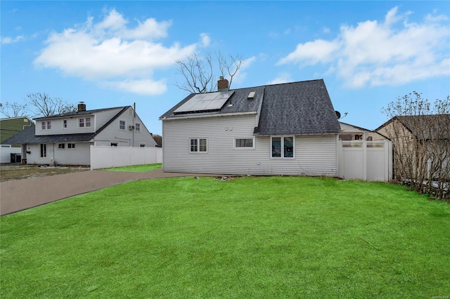 rear view of property featuring solar panels and a lawn