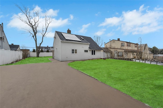 rear view of property featuring a yard and solar panels