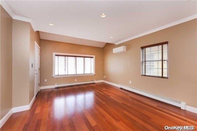 unfurnished room featuring an AC wall unit, plenty of natural light, dark wood-type flooring, and a baseboard heating unit