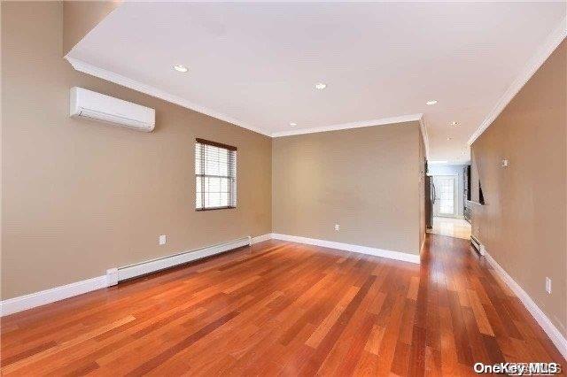 empty room with hardwood / wood-style flooring, a wall unit AC, a baseboard heating unit, and crown molding