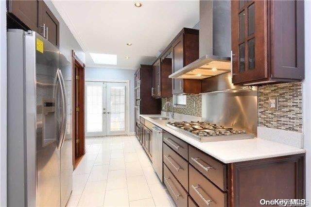 kitchen with french doors, wall chimney exhaust hood, sink, decorative backsplash, and appliances with stainless steel finishes