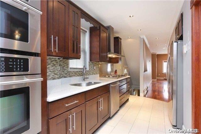 kitchen featuring sink, wall chimney exhaust hood, stainless steel appliances, light hardwood / wood-style flooring, and decorative backsplash