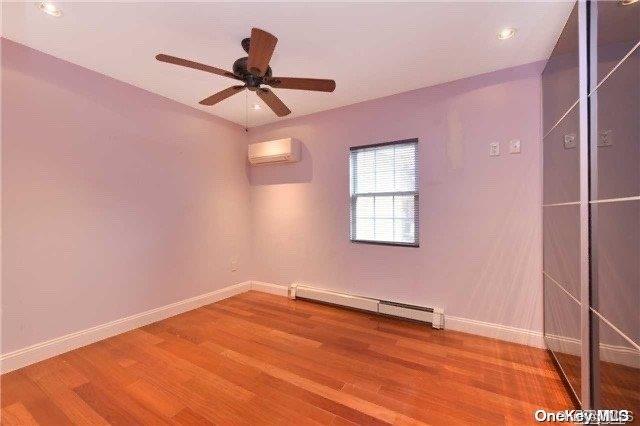 unfurnished room featuring baseboard heating, ceiling fan, hardwood / wood-style floors, and a wall unit AC