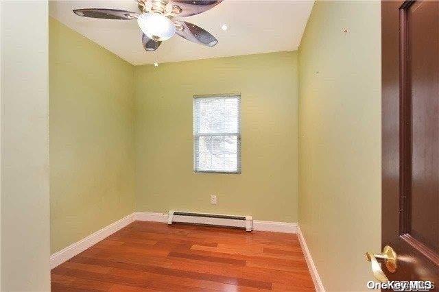 spare room featuring ceiling fan, hardwood / wood-style floors, and a baseboard heating unit