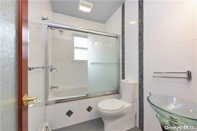 bathroom with toilet, combined bath / shower with glass door, and tile walls