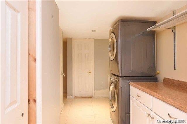 clothes washing area featuring stacked washer / drying machine, light tile patterned flooring, and cabinets