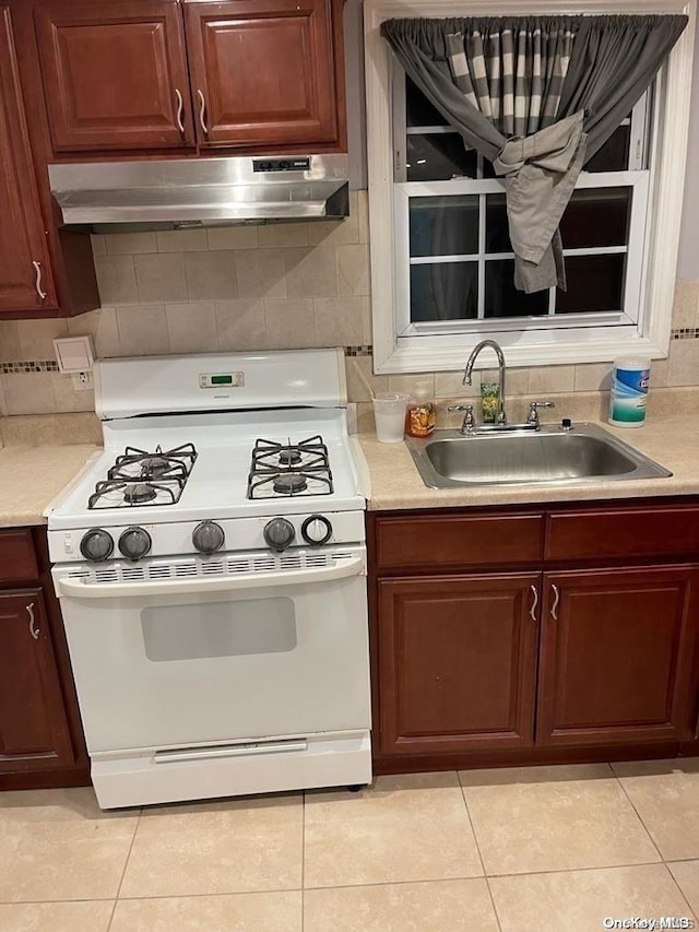 kitchen with decorative backsplash, light tile patterned flooring, white range with gas stovetop, and sink