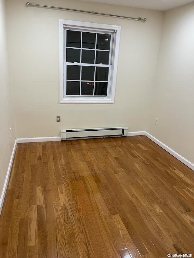 spare room featuring baseboard heating and wood-type flooring