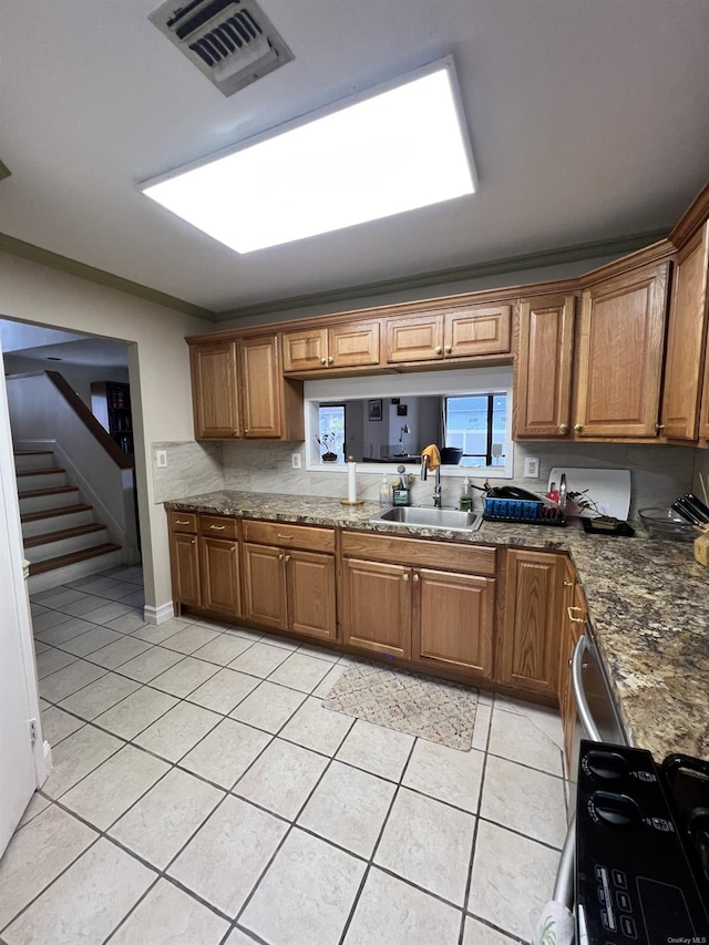 kitchen with dark stone countertops, crown molding, light tile patterned floors, and sink