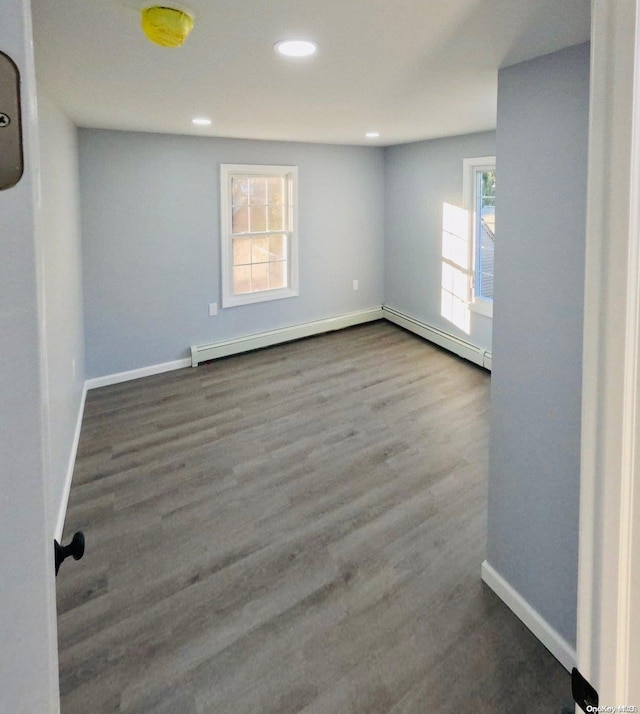 spare room featuring baseboard heating, a wealth of natural light, and hardwood / wood-style floors