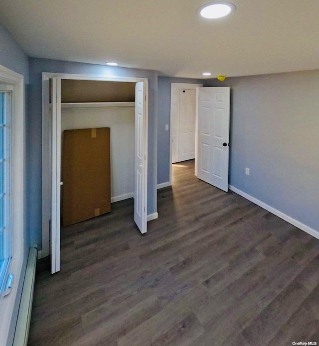 unfurnished bedroom featuring a closet, dark hardwood / wood-style flooring, and a baseboard heating unit