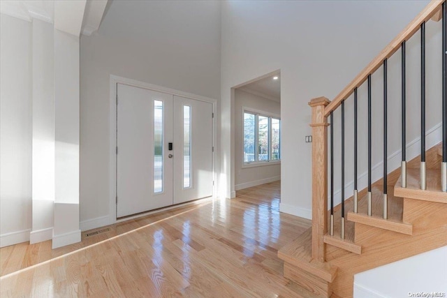 entrance foyer featuring light hardwood / wood-style floors, a towering ceiling, and crown molding