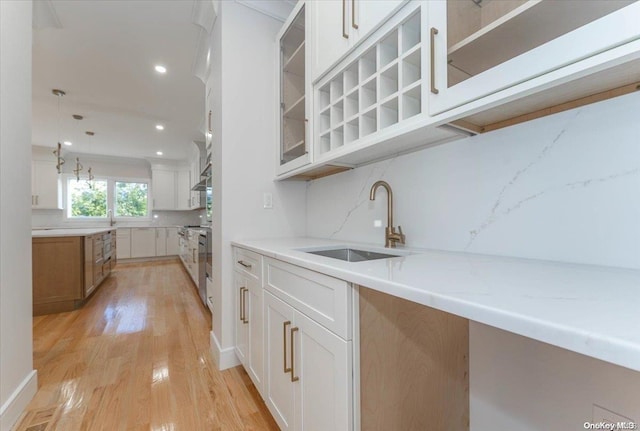 kitchen featuring white cabinets, light hardwood / wood-style floors, light stone countertops, and sink