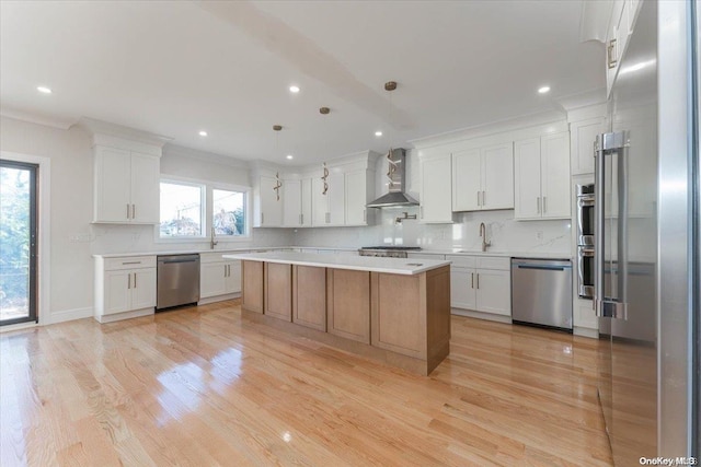 kitchen featuring white cabinetry, a large island, wall chimney exhaust hood, stainless steel appliances, and decorative light fixtures