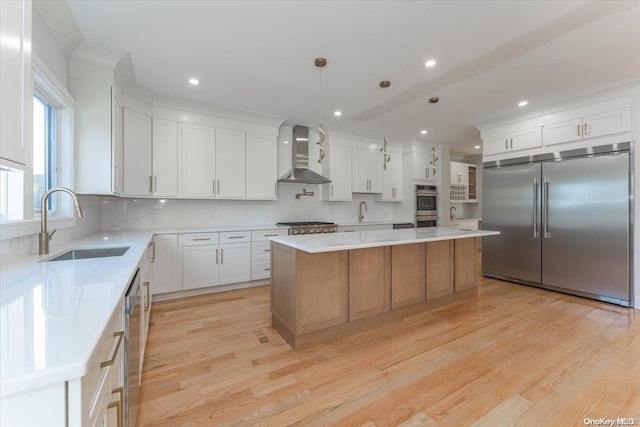 kitchen with a center island, wall chimney exhaust hood, pendant lighting, white cabinets, and appliances with stainless steel finishes