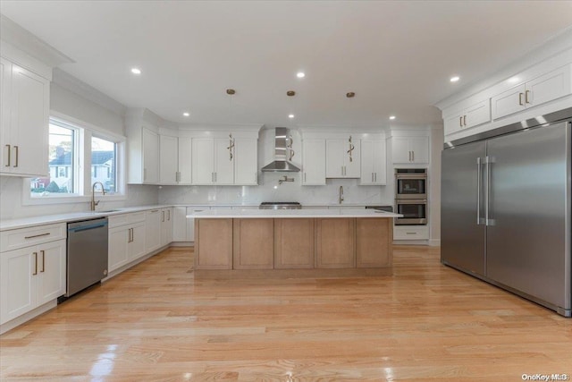 kitchen with stainless steel appliances, wall chimney range hood, decorative light fixtures, white cabinets, and a center island