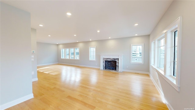 unfurnished living room featuring a wealth of natural light, a premium fireplace, and light wood-type flooring