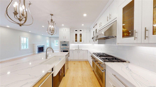 kitchen featuring light stone countertops, white cabinetry, pendant lighting, appliances with stainless steel finishes, and light wood-type flooring