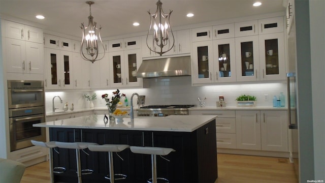 kitchen with decorative backsplash, appliances with stainless steel finishes, sink, white cabinetry, and an island with sink