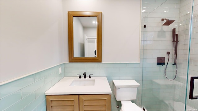 bathroom with a tile shower, vanity, tile walls, and toilet