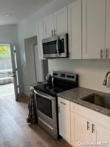 59 Port Washington Ave, Sound Beach, NY 11789 - kitchen with appliances with stainless steel finishes, a sink, wood finished floors, dark stone countertops, and white cabinets