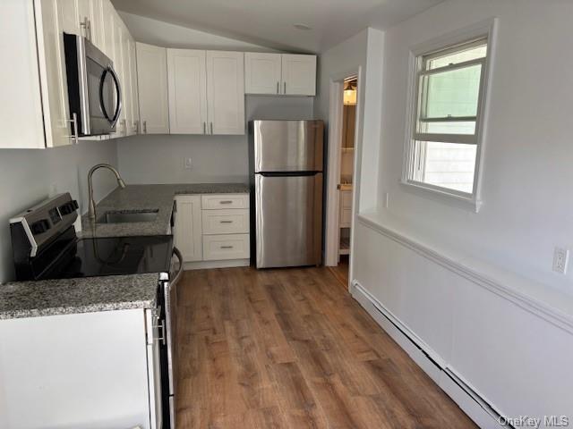 59 Port Washington Ave, Sound Beach, NY 11789 - kitchen with appliances with stainless steel finishes, a sink, white cabinets, baseboard heating, and wood finished floors