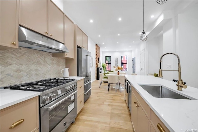 kitchen with pendant lighting, high end appliances, sink, tasteful backsplash, and light hardwood / wood-style floors