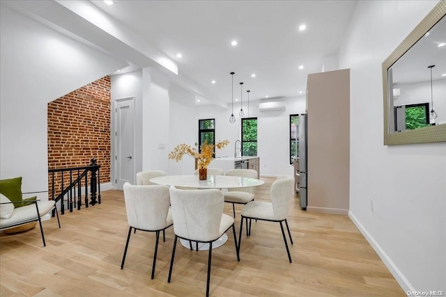 dining area with a wall unit AC, sink, and light wood-type flooring