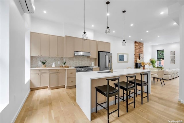 kitchen with premium appliances, light hardwood / wood-style flooring, an AC wall unit, an island with sink, and decorative light fixtures