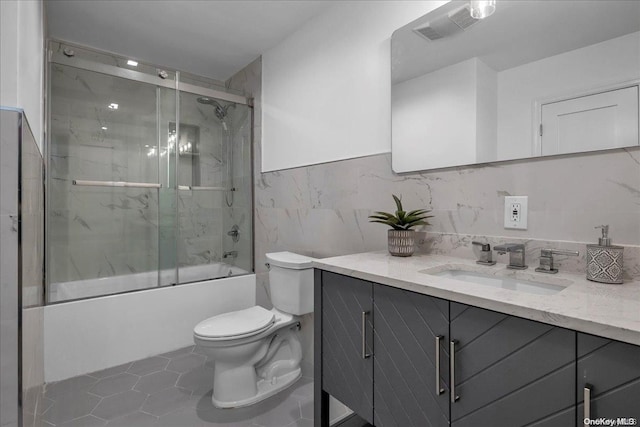 full bathroom with tile patterned floors, bath / shower combo with glass door, vanity, tile walls, and toilet