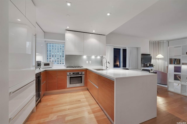 kitchen featuring white cabinets, sink, light wood-type flooring, kitchen peninsula, and stainless steel appliances