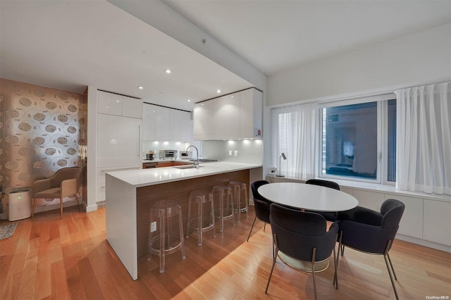 kitchen with white cabinets, light hardwood / wood-style floors, kitchen peninsula, and a breakfast bar area