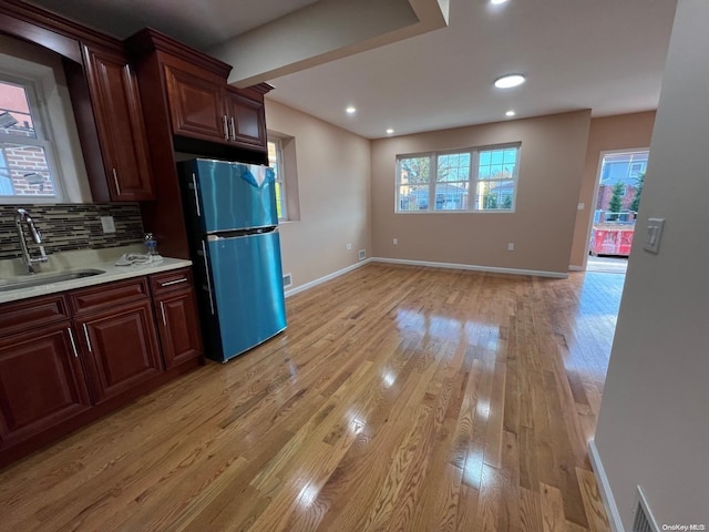 kitchen with tasteful backsplash, stainless steel fridge, sink, and light hardwood / wood-style floors